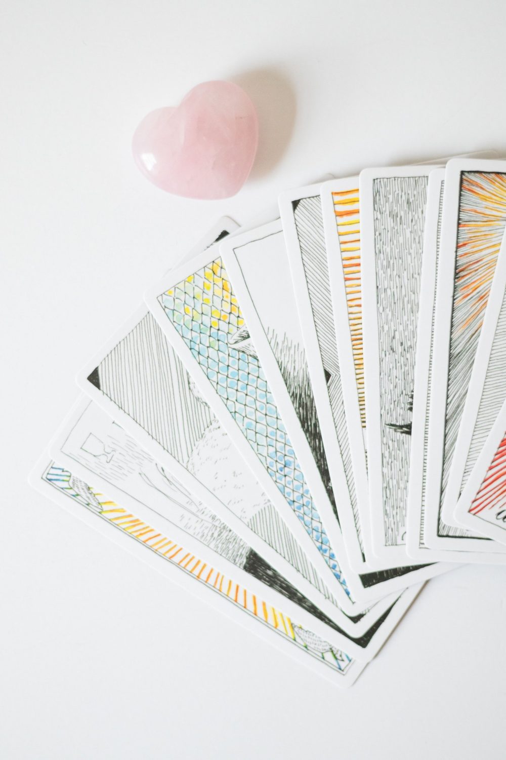 Cartas de tarot en abanico junto a un cuarzo rosa en forma de corazón sobre una mesa blanca